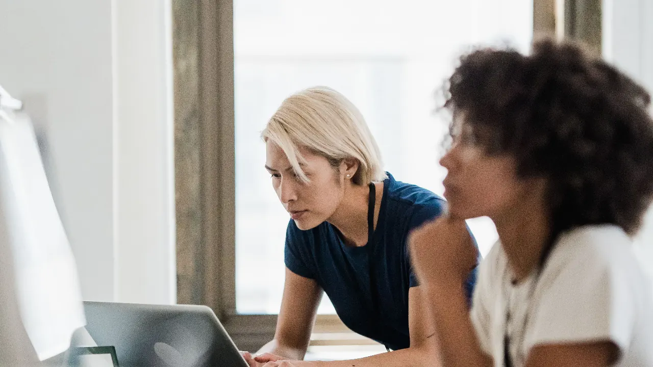 Two women working together on a laptop by a window